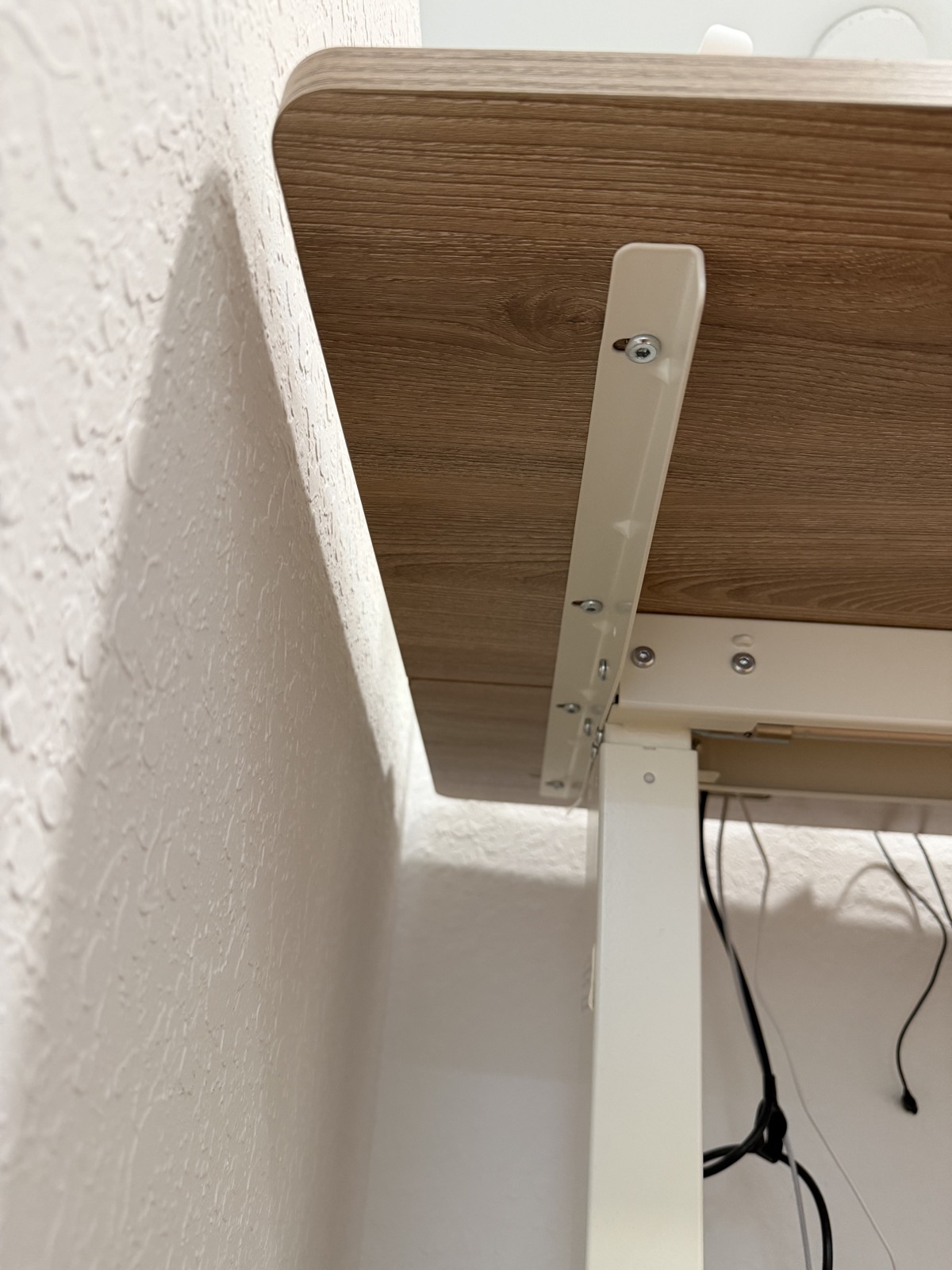 Underside view of the SHW desk showing the frame rail and fasteners holding the desktop to the standing desk frame.
