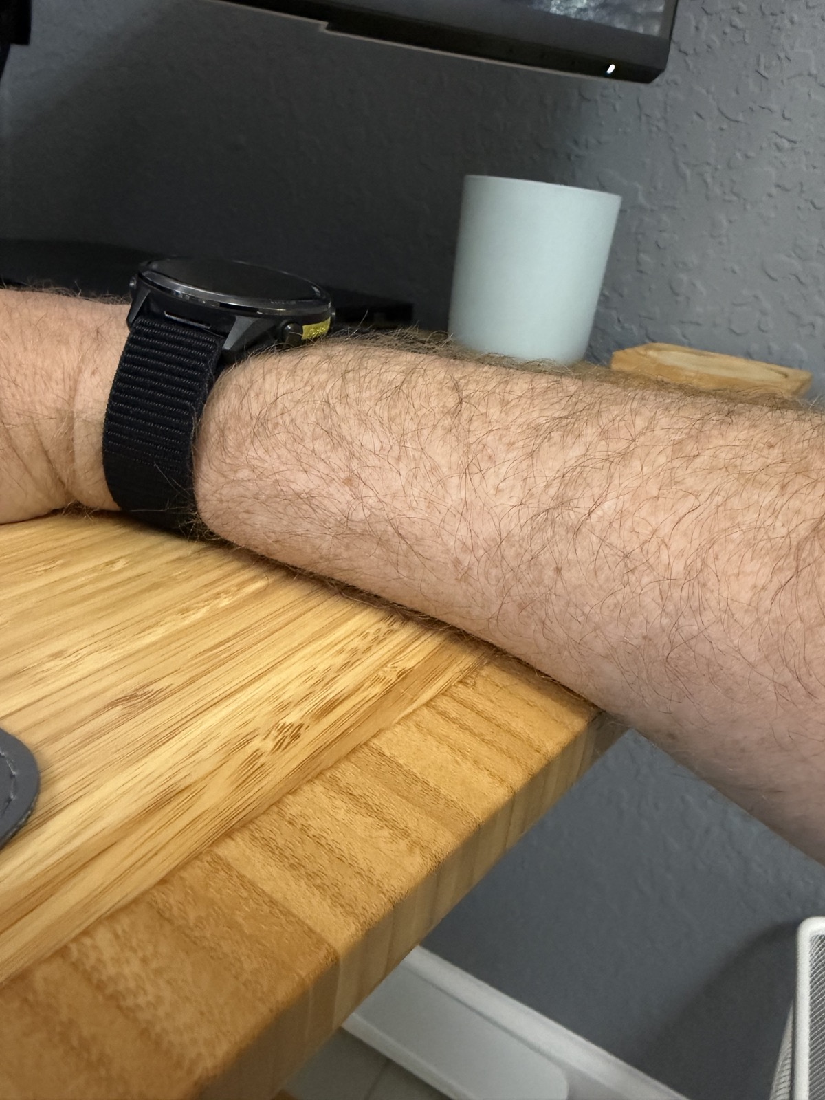 A forearm resting on the rounded bamboo curve of the UPLIFT standing desk.