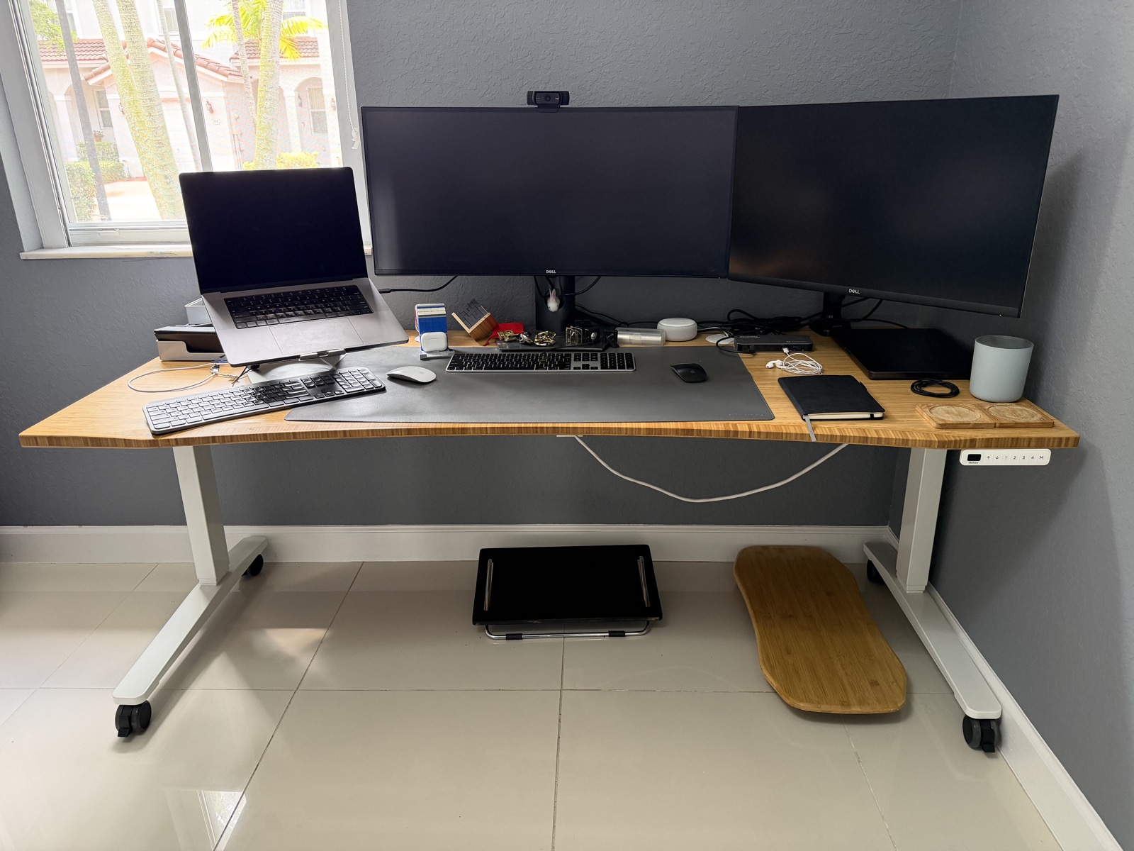A 72 by 30 inch UPLIFT standing desk with a bamboo curved front, white frame, laptop, dual monitors, keyboard, mouse, and desk mat.